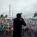 Artist Murkage on stage at Colour Clash 2024. The view is from behind him, overlooking the crowd