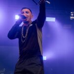 Artist Murkage on stage at Colour Clash 2024. He is wearing two gold chains, has the microphone to his mouth and there is deep blue lighting in the background