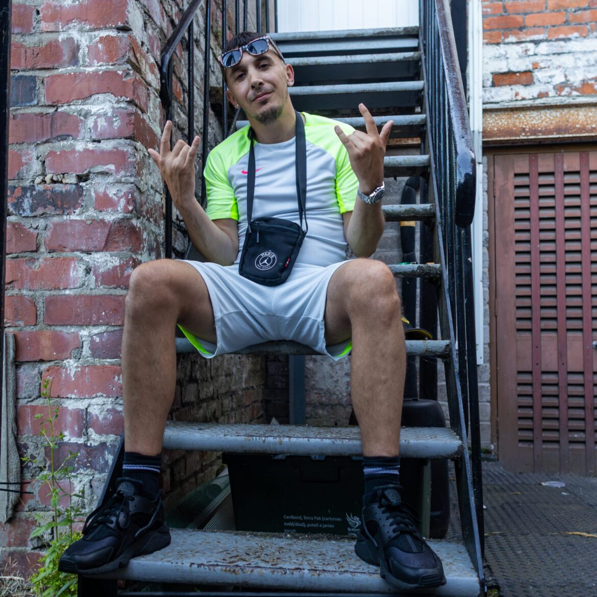 Artist Murkage sat on steps outside Play it Loud Studio. The image is cropped to a 1x1 square